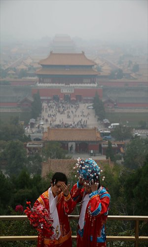 Two tourists wear traditional Chinese costumes to pose for pictures in Jingshan Park in Beijing on Sunday. The Forbidden City behind them is wrapped by heavy smog. Photo: Xinhua