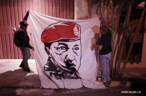 Residents hold a banner with the image of Venezuelan President Hugo Chavez after the news of Venezuelan President Hugo Chavez's death was released, in Tegucigalpa, Honduras, on March 5, 2013. Venezuelan President Hugo Chavez died on March 5. (Xinhua/Pedro Mera)