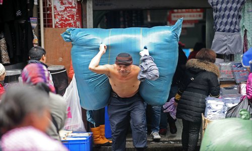 A shirtless porter carrying a huge bundle of goods bites down on a piece of wood in a commercial street in Wuhan, Hubei Province Saturday, as the temperature in the city dipped to 0 C. Photo: CFP
