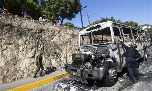 A Federal Police officer takes pictures in the crime scene after a bus was set ablaze in Mozimba neighborhood, Acapulco, Guerrero State, Mexico on Wednesday. The bus was attacked by unknown gunmen who evacuated passengers and killed the driver and his 14-year-old assistant before setting fire to the bus. Photo: AFP