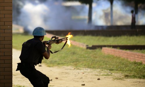 A Bangladeshi policeman fires a shotgun during clashes with garment workers in Ashulia on Tuesday. Production in some 200 garment factories in Ashulia was suspended as workers fought police demanding implementation of the new minimum wages recommended by a government-appointed wage board. Photo: AFP