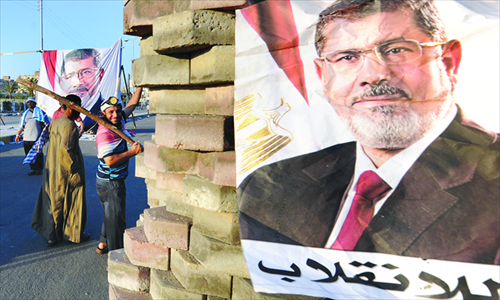 Supporters of the Muslim Brotherhood gesture as they stand close to an image of deposed president Mohamed Morsi at a makeshift brick barricade erected along a main street in Nasr City, a district of eastern Cairo, on Sunday, as supporters of Morsi continue to hold a sit-in outside Rabaa al-Adawiya mosque demanding his reinstatement. Photo: AFP