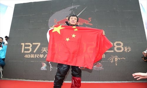A weary but victorious Guo Chuan holds up a flag after completing his single-handed sail around the world. 