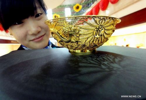 A staff member shows a set of gold tableware at a gold store in Jinan, capital of east China's Shandong Province, August 20, 2012. The set of tableware sells at 14,000 RMB ($2200). Photo: Xinhua