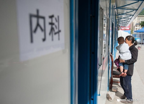 A woman carrying her child waits for seeing a doctor outside a temporarily-erected prefabricated house at the People's Hospital in Lushan County, southwest China's Sichuan Province, May 12, 2013. Eight prefabricated houses have been built here to provide medical services to residents. The county was jolted by a 7.0-magnitude earthquake on April 20. (Xinhua/Li Hualiang) 