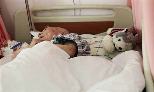 An elderly man lies in bed with a toy dog at Linfen Community Health Center in May. Photo: CFP