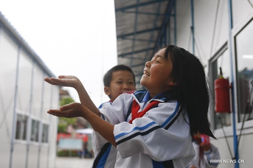 A student of the central primary school of Shangli Town enjoys the rain outside a makeshift classroom in Shangli, Lushan County, southwest China's Sichuan Province, May 16, 2013. The schoolhouses of the Shangli Town Center School were destroyed in the 7.0-magnitude earthquake taken place in Lushan on April 20, leaving more than 1, 200 students to have classes in newly built prefab houses. (Xinhua/Liu Xiao)&nbsp; 