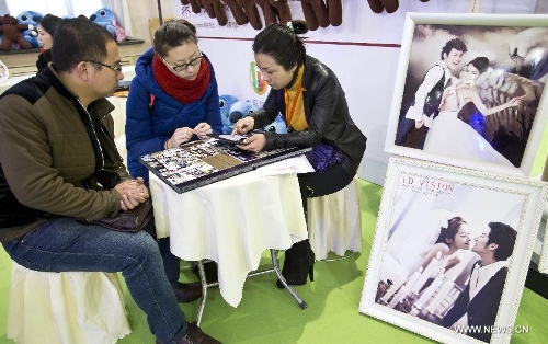 A working staff (R) introduces wedding photography services to visitors during the 2013 Beijing Wedding Expo in Beijing, capital of China, March 1, 2013. The three-day event kicked off on Friday. (Xinhua/Wang Jingsheng) 