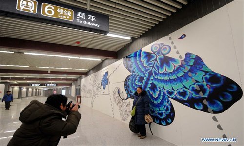 A passenger poses for photos in front of a wall painting at the Nanluoguxiang Station of the newly-opened subway line 6 in Beijing, capital of China, December 30, 2012