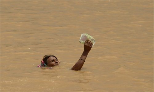 A flood-affected villager holds an item above water as she attempts to reach higher ground on the outskirts of Patna in northeastern India on Wednesday. The monsoon, which covers the subcontinent from June to September and usually brings flooding, accounts for about 80 percent of India's annual rainfall. Photo: AFP