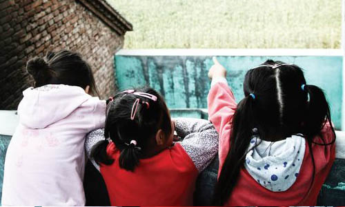 Three schoolgirls look out from a balcony after school in Caomiao village of rural Luoyang, Henan Province on May 21. Many students in the village are 
