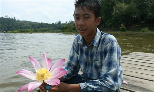 A young man holds a lotus flower along the water. Photo: CFP