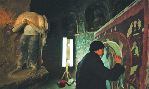 Painter Wu Shuangqin copies a wall painting in a cave of the Mogao Grottoes. Photo: CFP