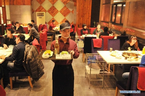 A working staff serves the dishes at a hot pot restaurant in Lanzhou, capital of northwest China's Gansu Province, Jan. 30, 2013. A 