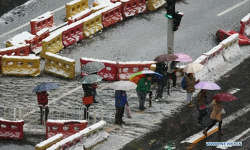 Residents shelter from sleet under umbrellas on the Xingfu Street in Beijing, capital of China, on November 4, 2012. The capital city had witnessed snowfall and sleet since Saturday night as cold current swept north China and dropped temperature. Photo: Xinhua