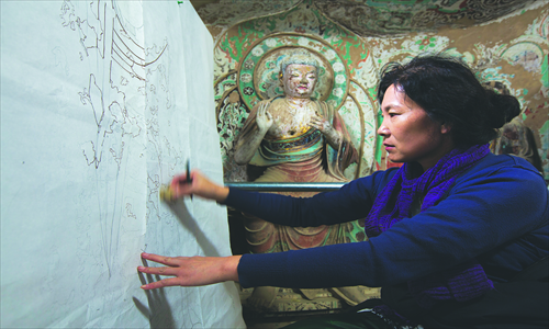 Guan Jinwen, who went to the institute in 1983, works on her copy in a cave of the Mogao Grottoes. Photo: CFP