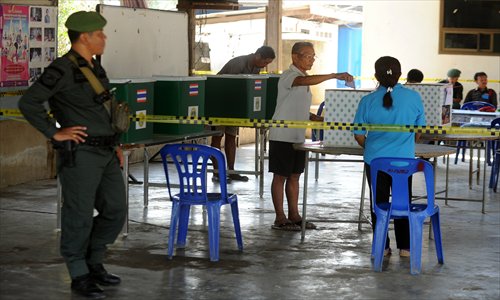 A police official (left) keeps a watch as a Thai voter (center) casts his vote into the ballot box at the Taa Ta Kho village polling station as part of a re-run of general elections in the village in Petchaburi province, south of Bangkok on Sunday. Photo: AFP