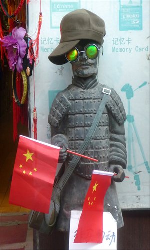 A sculpture of terracotta warrior wearing a hat and sunglasses stands in front of a store on Beijing's Skewed Tobacco Pouch Street, holding Chinese national flags and a shopping bag on Friday. Photo: CFP