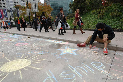 A man chalk-draws on the pavement during first Chalkupy Vancouver event in Vancouver, Canada, on September 22, 2012. People from all walks of life descend on Robson Street in downtown Vancouver at noon to create beautiful sidewalk chalk art together. Photo: Xinhua