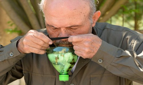 A picture taken on Friday shows Abu Tarek, a 74-year-old retired army officer, trying on a homemade gas-mask assembled using a plastic bottle, coal, cotton, gauze, cola, and cardboard, for protection against chemical weapons, in Syria's northern Latakia province. Photo: AFP   