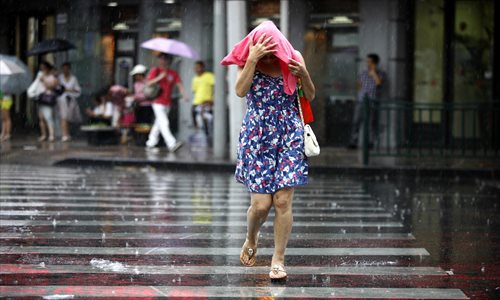 A pedestrian shields herself from the rain after a thunderstorm suddenly hit the city Thursday afternoon. The local weather bureau issued an orange rain storm alert. Meanwhile, the temperature fell below 30 C. Photo: Cai Xianmin/GT