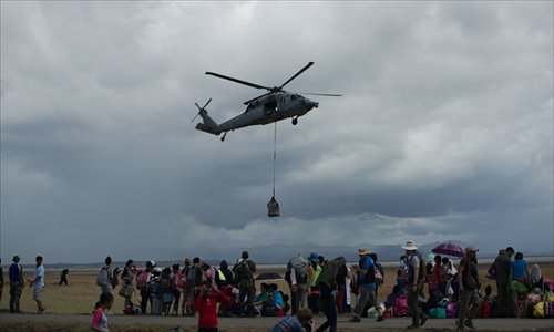 Local residents watch as a US navy helicopter delivers relief supplies at Tacloban airport on Thursday. Scores of decaying bodies were being taken to mass graves as overwhelmed Philippine authorities grappled with disposal of the dead and the living begged for help in the aftermath of the disaster. Photo: AFP
