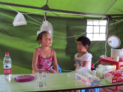 Children sit in a relief tent in Wangzuo village in Fengtai district, an area hit by flooding on July 21. More than 34 households are still living in tents, which have TV sets for people to watch the Olympic Games. Photo: CFP