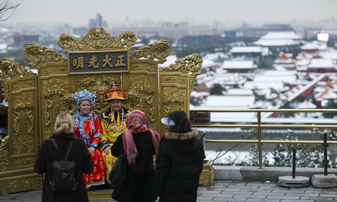 Foreigners take pictures sitting on a replica “dragon seat” in Jingshan Park in Beijing. Photo: CFP