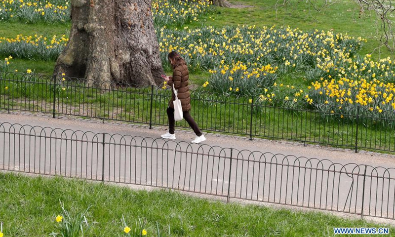 A woman walks by flowers in a park in central London, Britain, on March 25, 2021.Photo:Xinhua