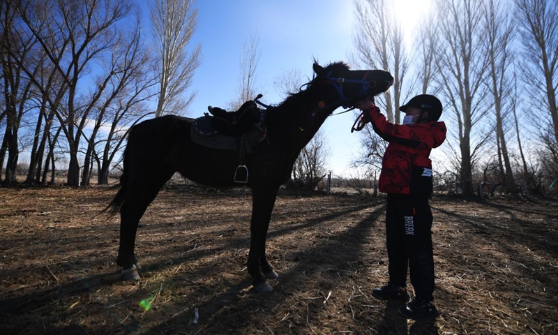 Yernar Tiemerbek, a senventh grade student of Oymak Boarding School, touches a horse during an equestrian class in Burqin County, northwest China's Xinjiang Uygur Autonomous Region, March 30, 2021. Photo: Xinhua