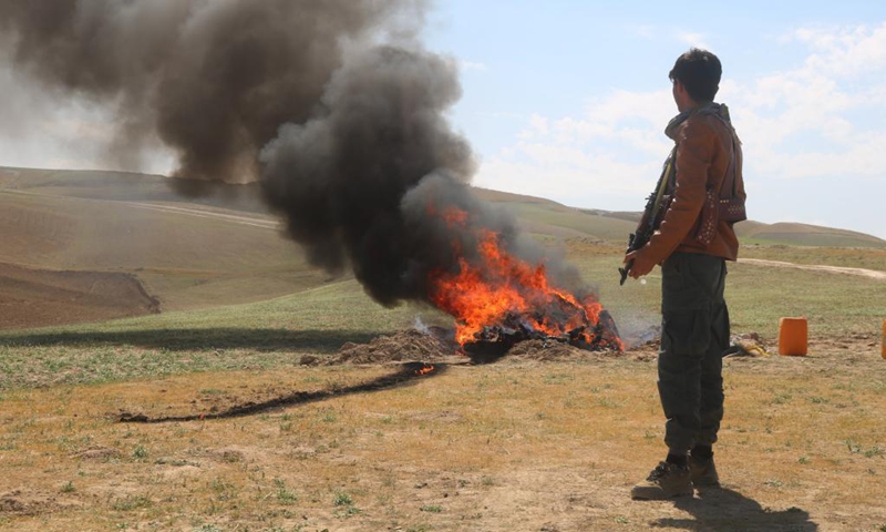 An Afghan policeman stands guard as smoke rises from burning drugs in Sari Pul province, April 17,2021. The Afghan authorities burned about one ton of seized narcotic drugs in Sari Pul province, Afghanistan, a local official said on Saturday. (Photo: Xinhua)