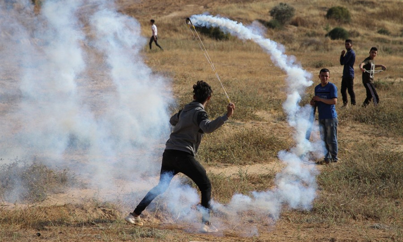 A Palestinian protester uses a slingshot to throw back a tear gas canister fired by Israeli troops during a protest against the violence in the Old City of Jerusalem, on the Gaza-Israel border, on May 8, 2021.(Photo: Xinhua)