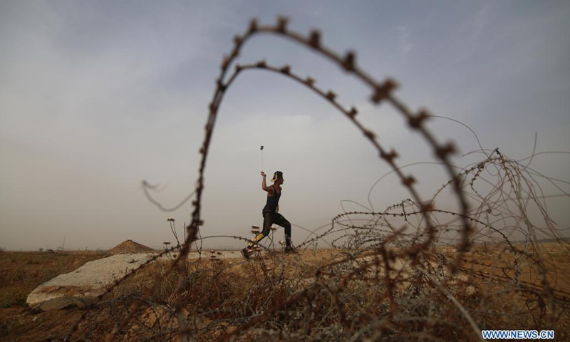 A Palestinian protester uses a slingshot to hurl a stone at Israeli troops during a protest against the violence in Jerusalem, on the Gaza-Israel border east of southern Gaza Strip city of Khan Younis, on May 9, 2021. About 290 Palestinians were injured over the weekend in clashes with Israel's police at the Al-Aqsa Mosque compound and other parts of East Jerusalem.(Photo: Xinhua)