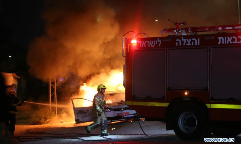 An Israeli firefighter works near a burning police car in Lod, central Israel, on May 12, 2021. Israeli police announced on Wednesday that a night curfew will be imposed in Lod, where clashes between Arabs and Jews have been spiraling for days.(Photo: Xinhua)