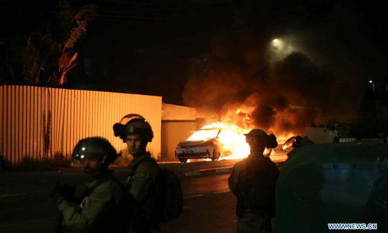 Israeli security force members stand guard near a burning police car in Lod, central Israel, on May 12, 2021. Israeli police announced on Wednesday that a night curfew will be imposed in Lod, where clashes between Arabs and Jews have been spiraling for days.(Photo: Xinhua)