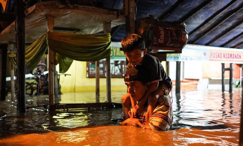 A father carrying his son on shoulders walks through flood water due to the overflow of Deli river at Medan in North Sumatra, Indonesia, on May 15, 2021.Photo:Xinhua