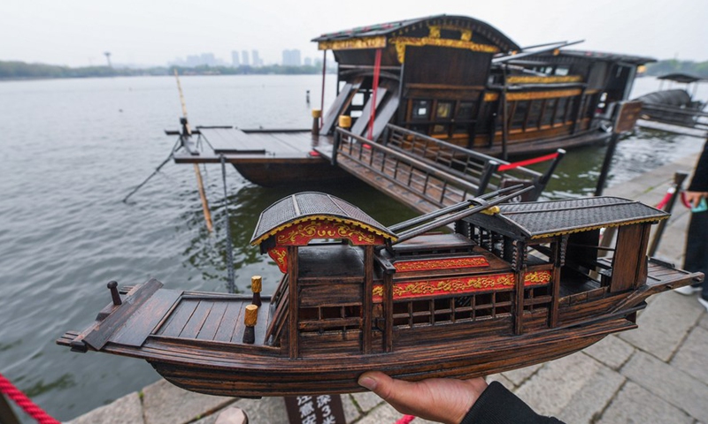 Han Minghua stands beside the Red Boat with a self-made Red Boat model in hand on the bank of the Nanhu Lake in Jiaxing City, east China's Zhejiang Province, April 13, 2021.(Photo: Xinhua)