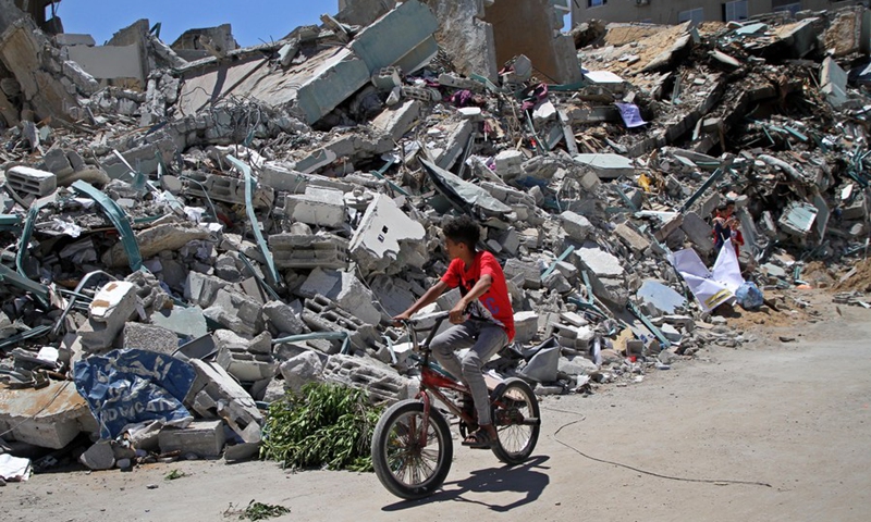 A Palestinian boy rides his bicycle past the rubble of Jala Tower destroyed during an Israeli air strike in Gaza City, May 23, 2021.(Photo: Xinhua)