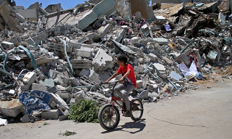 A Palestinian boy riding a bicycle passes by the ruins of the Jala Tower destroyed by Israeli airstrikes, in Gaza City, on May 23, 2021.(Photo: Xinhua)