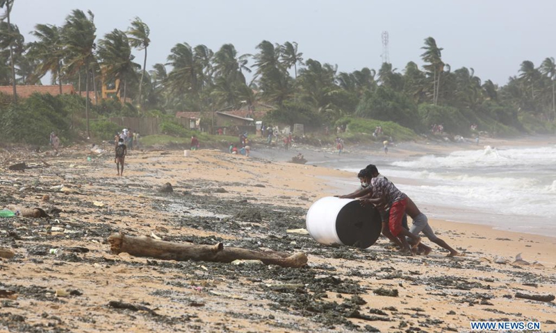People roll a piece of item washed off to the shore from the burning foreign ship X-Press Pearl at Kapungoda, outskirts of Colombo, Sri Lanka, May 26, 2021. Sri Lankan authorities said on Wednesday it is monitoring an oil spill from a burning foreign vessel near the Port of Colombo, warning that the oil spill may waft towards the Negombo lagoon in the west coast of the country. (Photo: Xinhua)