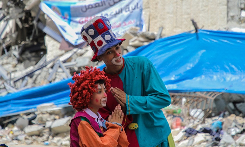 Palestinian volunteers dressed as clowns interact with children, near the ruins of Hanady Tower which was targeted by Israeli warplanes, in Gaza City, May 31, 2021.(Photo: Xinhua)