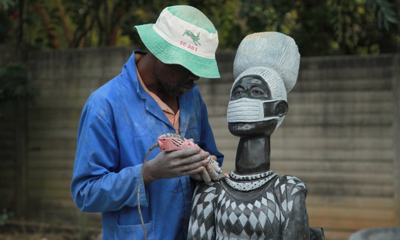 A man works on a piece of stone sculpture showcasing a woman wearing a face mask in Harare, Zimbabwe, on June 8, 2021.(Photo: Xinhua)