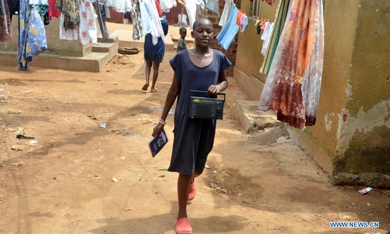 A girl carrying a radio walks in a neighborhood in Kampala, Uganda, June 14, 2021. Radio lessons for students in middle grades of primary schools in Uganda resumed on Monday following the closure of schools due to the COVID-19 pandemic. (Photo: Xinhua)