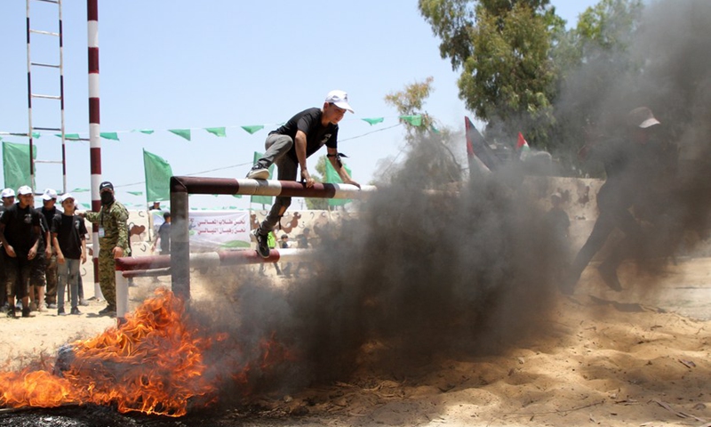A Palestinian boy climbs over the burning barrier at a military summer camp run by Hamas at the Al-Yarmouk military site, east of Gaza City, on June 26, 2021.(Photo: Xinhua)