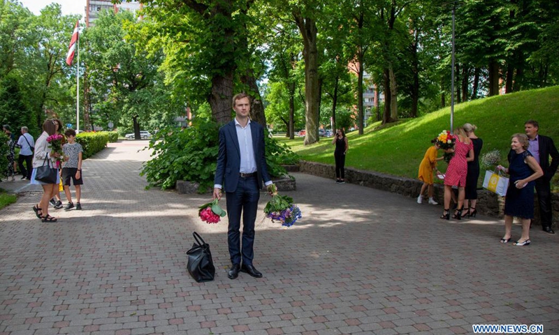 People hold bunches of flowers to wait for students attending a graduation ceremony outside Riga Stradins University in Riga, Latvia, on June 29, 2021.(Photo: Xinhua)