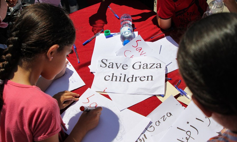 Palestinian children write SOS messages of Save Gaza Children on paper, at the fishing port in Gaza City, on June 30, 2021.(Photo: Xinhua)