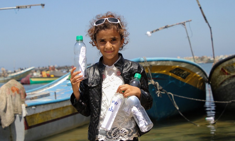 A Palestinian girl holds bottles with a message inside before tossing them into the sea, at the fishing port in Gaza City, on June 30, 2021.(Photo: Xinhua)