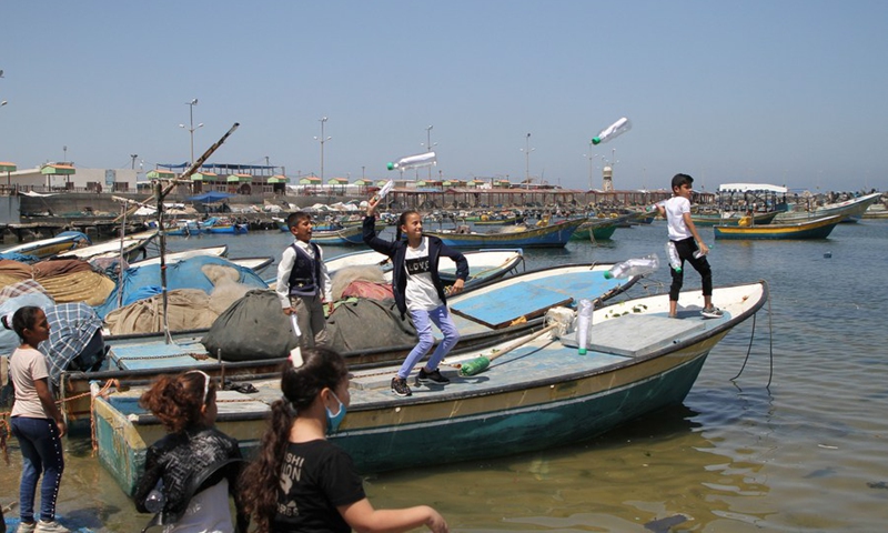 Palestinian children toss bottles with a message inside into the sea, at the fishing port in Gaza City, on June 30, 2021.(Photo: Xinhua)