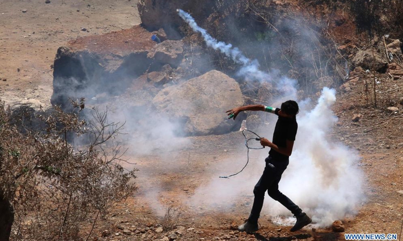 A protester throws back a tear gas canister fired by Israeli soldiers and members of Israeli border police following a protest against the expanding of Jewish settlements in the village of Beita, south of the West Bank city of Nablus, July 2, 2021.Photo:Xinhua