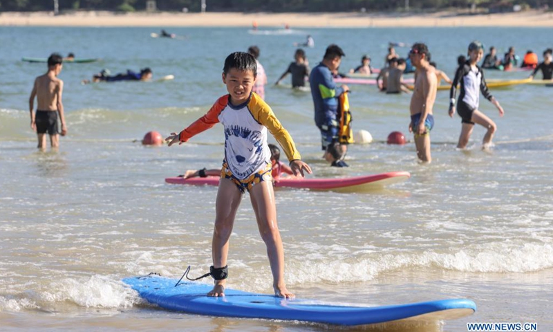 Tourists surf in the water of Tenghai fishing village in Sanya, south China's Hainan Province, July 8, 2021. Located in Haitang bay of Sanya, Tenghai fishing village has attracted lots of tourists by developing tourism, surfing and homestay industries since 2018.Photo:Xinhua